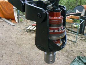 Nära bild av en hydraulisk rotator monterad på en maskinarm, används för arbete med skruvpålar.