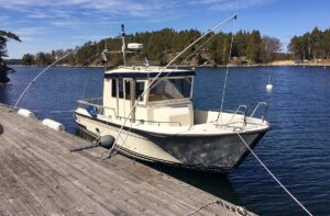 En vit motorbåt Targa 27 förtöjd vid en träbrygga med Mooring Whips i en vacker sjöomgivning.