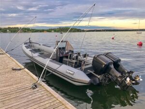 En Rupert ribb motorbåt med dubbla motorer förtöjd vid en brygga med Mooring Whips mot en solnedgångs backdrop.