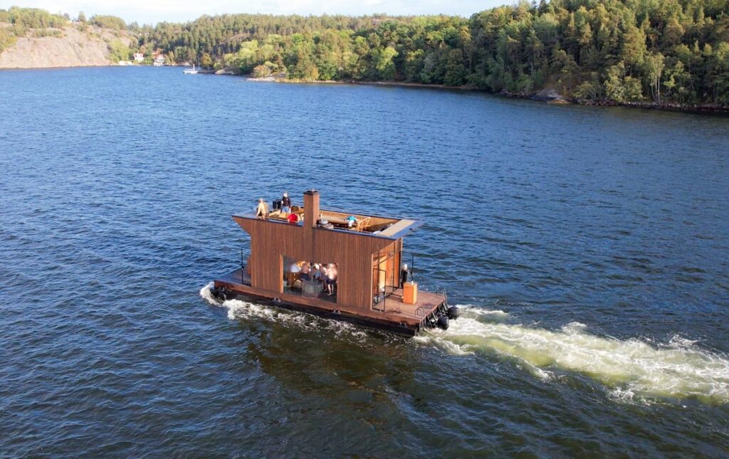 Kommersiell bastuflotte med gäster och vedeldad kamin på pontoner i rörelse på sjön