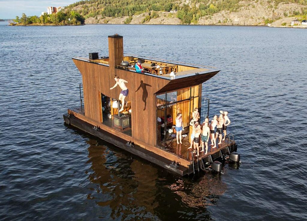 Bastuflotte med glada gäster som hoppar från taket i sjön