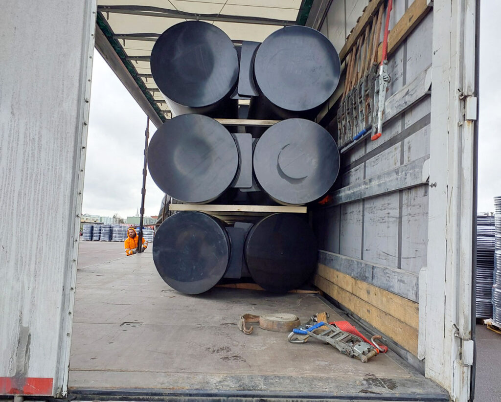 Seks 12 meter lange HDPE-flytepontonger sikret med transportstropper på lastebil før levering til Norge.